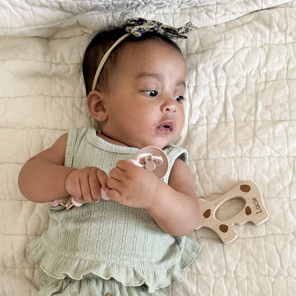 Baby lying on a textured surface with a wooden teether